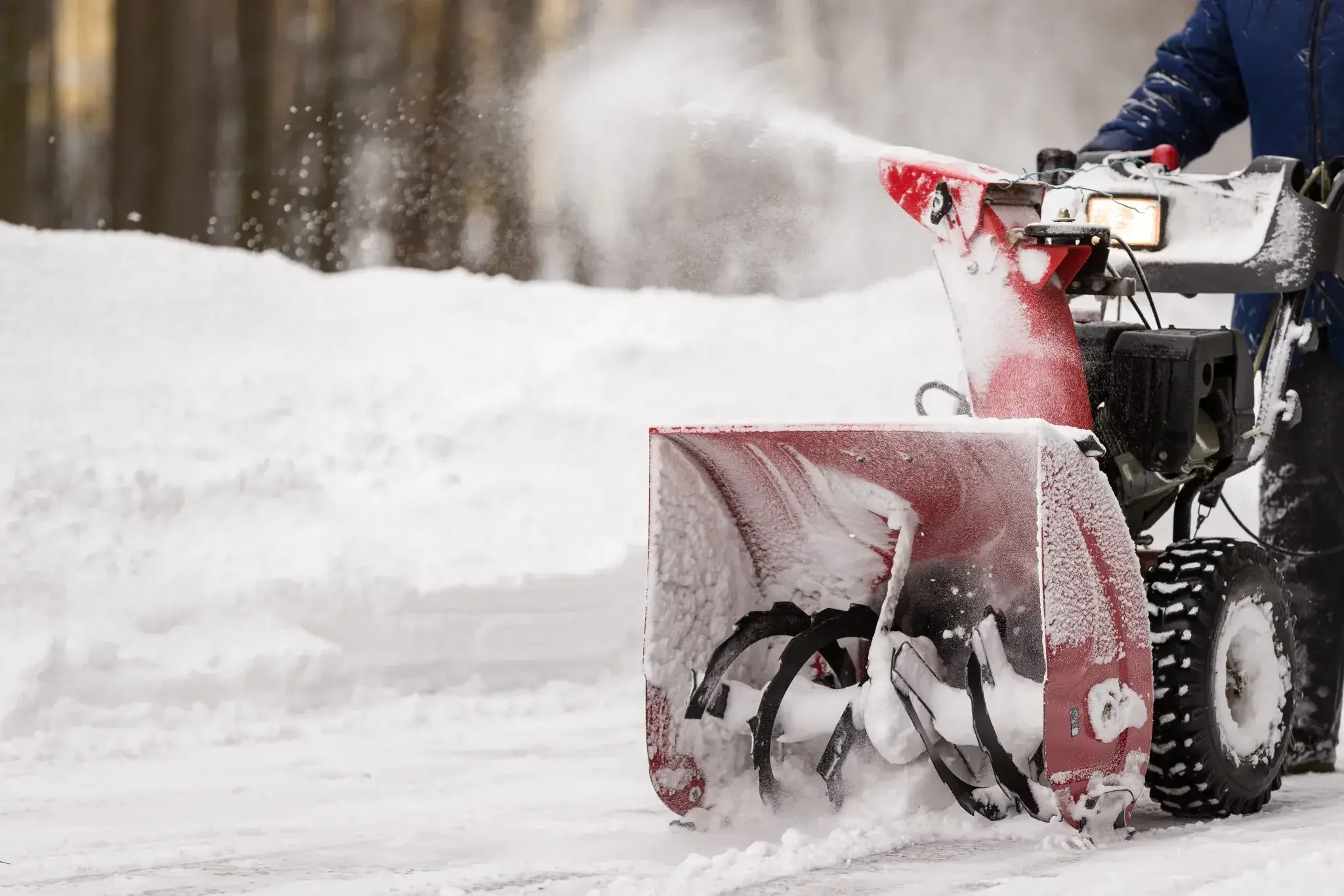 A person operating a snow blower in a snow-covered area during winter.