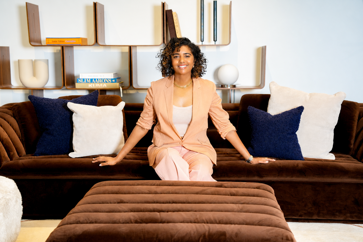 Woman sitting on a brown velvet sofa with pillows in a modern living room.