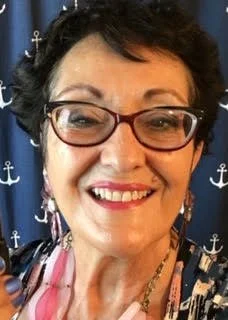 Loraine Joy, a smiling woman with short dark hair, glasses, earrings, and a patterned top.