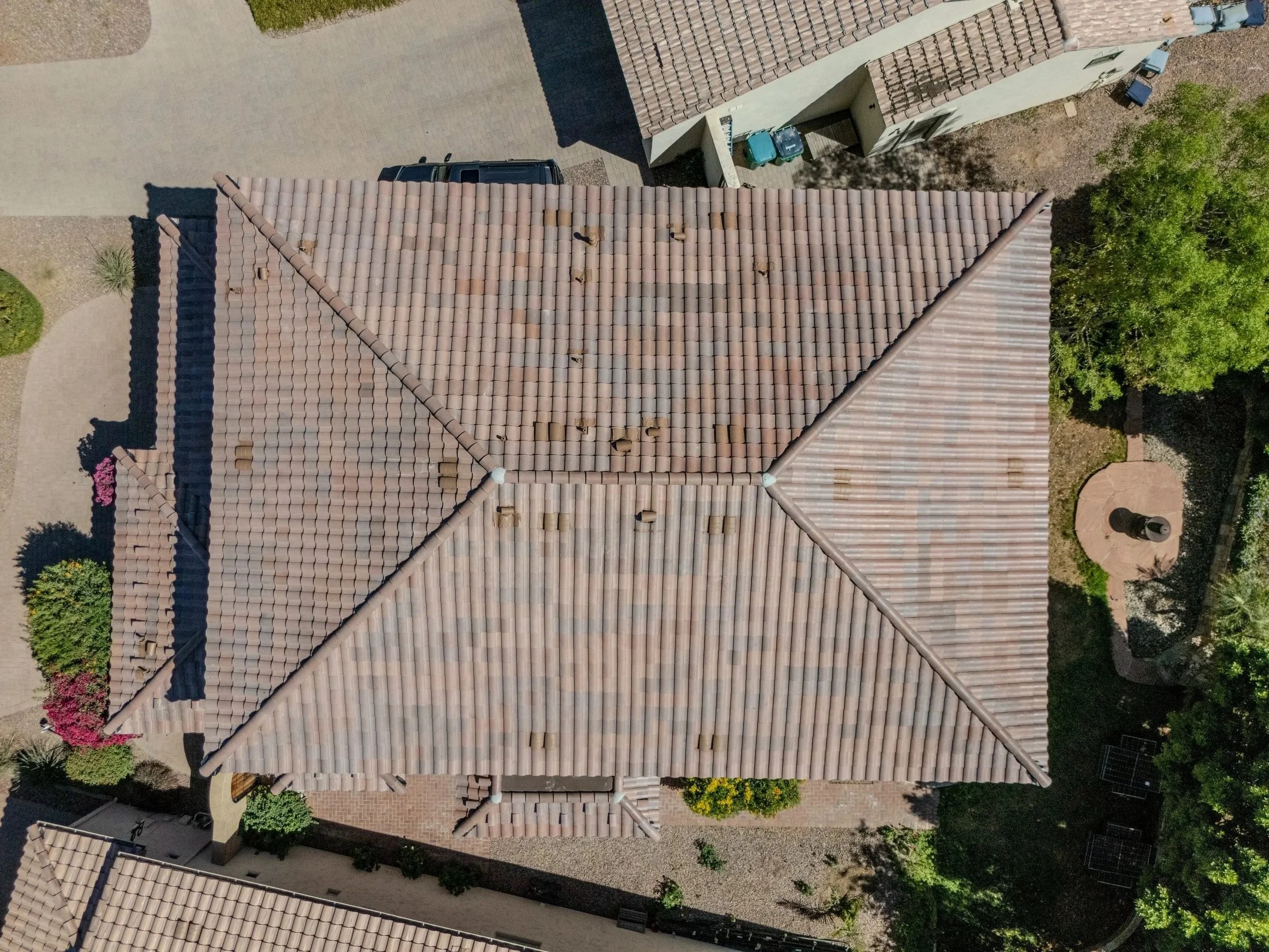 Aerial view of residential rooftops with tiled roofs, surrounding trees, a driveway, and landscaped yards.