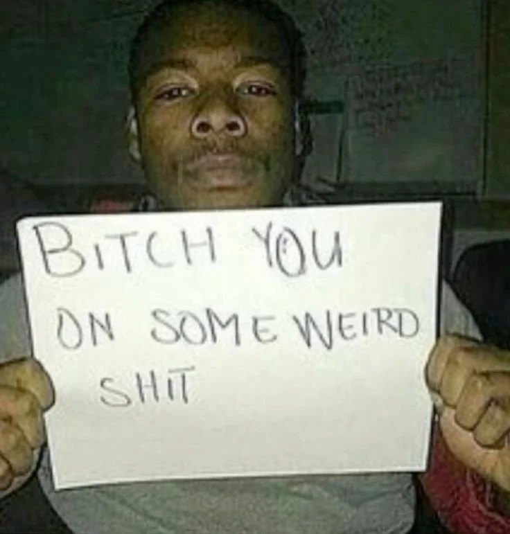 Young man with dreadlocks holding a sign that reads "Bitch you on some weird shit".