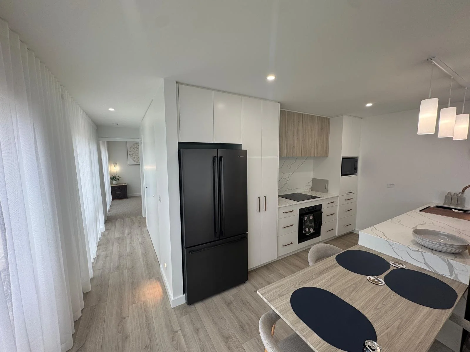 Modern kitchen with black refrigerator, white cabinetry, marble backsplash, and a dining table with black placemats and gray chairs.