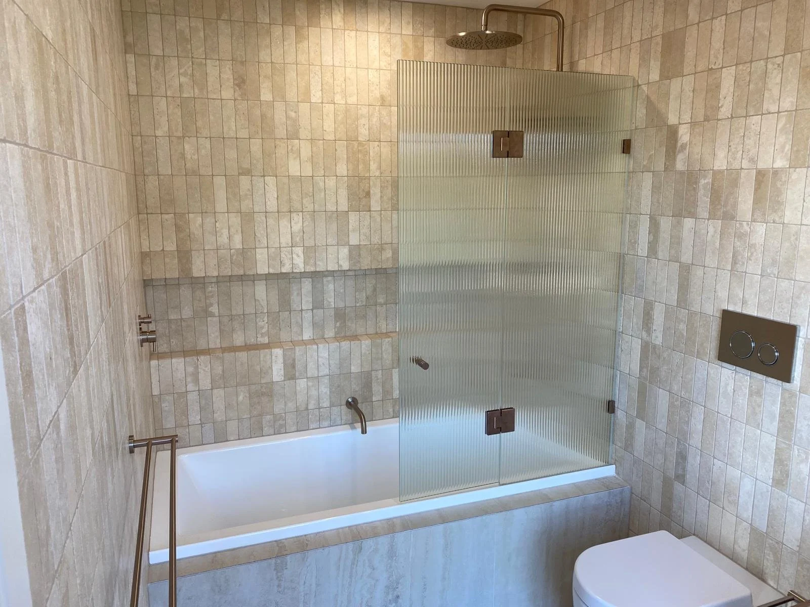 Modern bathroom with beige tiled walls and floor, a glass shower enclosure with textured glass, a rain shower head, a wall-mounted toilet, and a towel holder to the left.