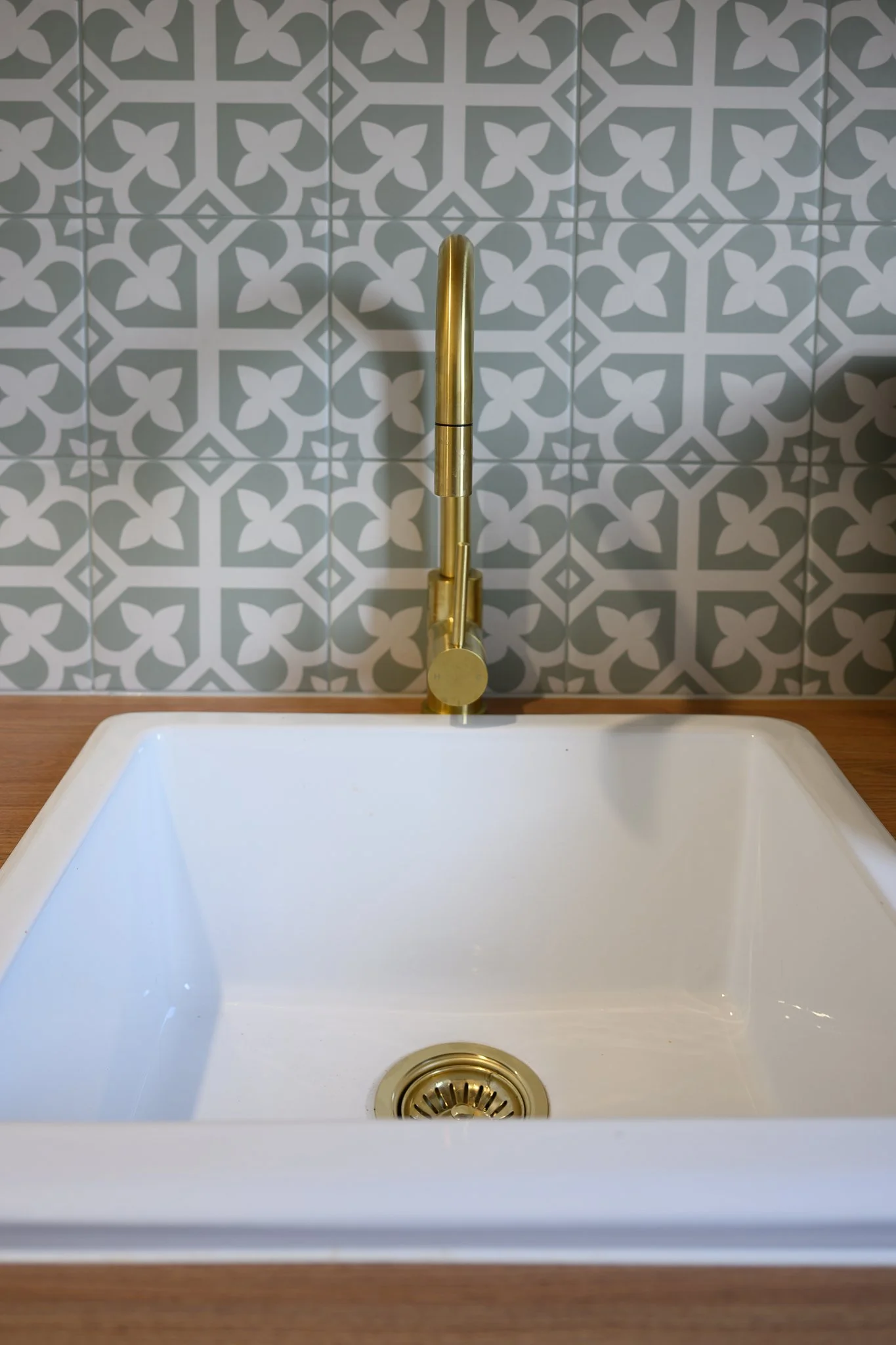 A white kitchen sink with a gold faucet and a patterned tile backsplash.
