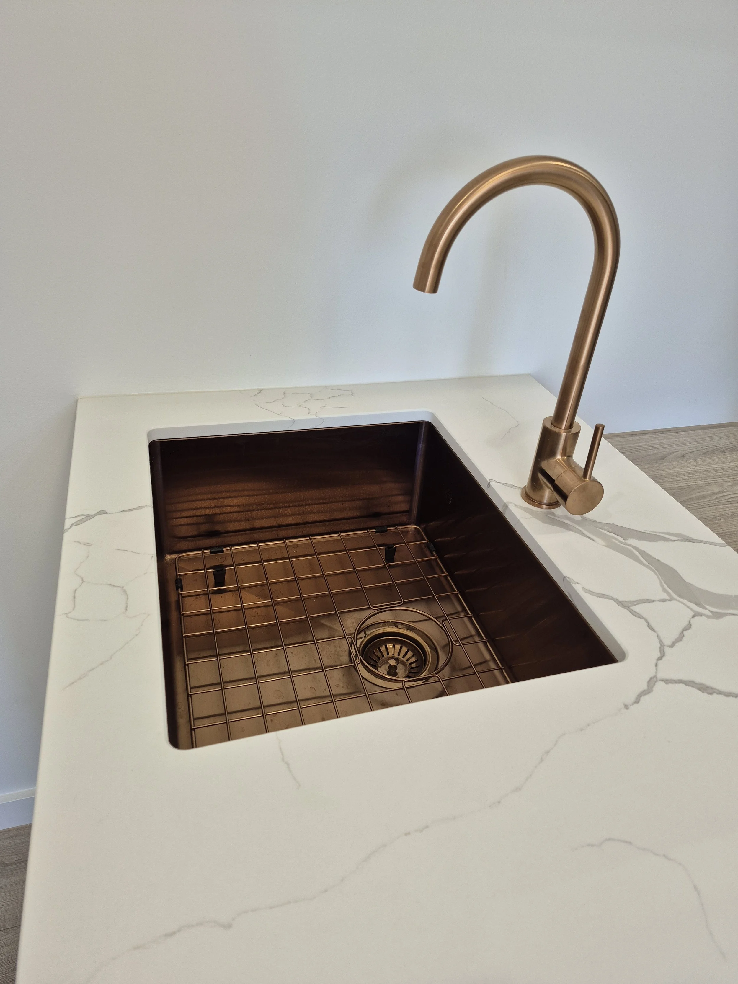 Close-up of a modern kitchen sink with a rose gold faucet and an empty marble countertop with gray veining.