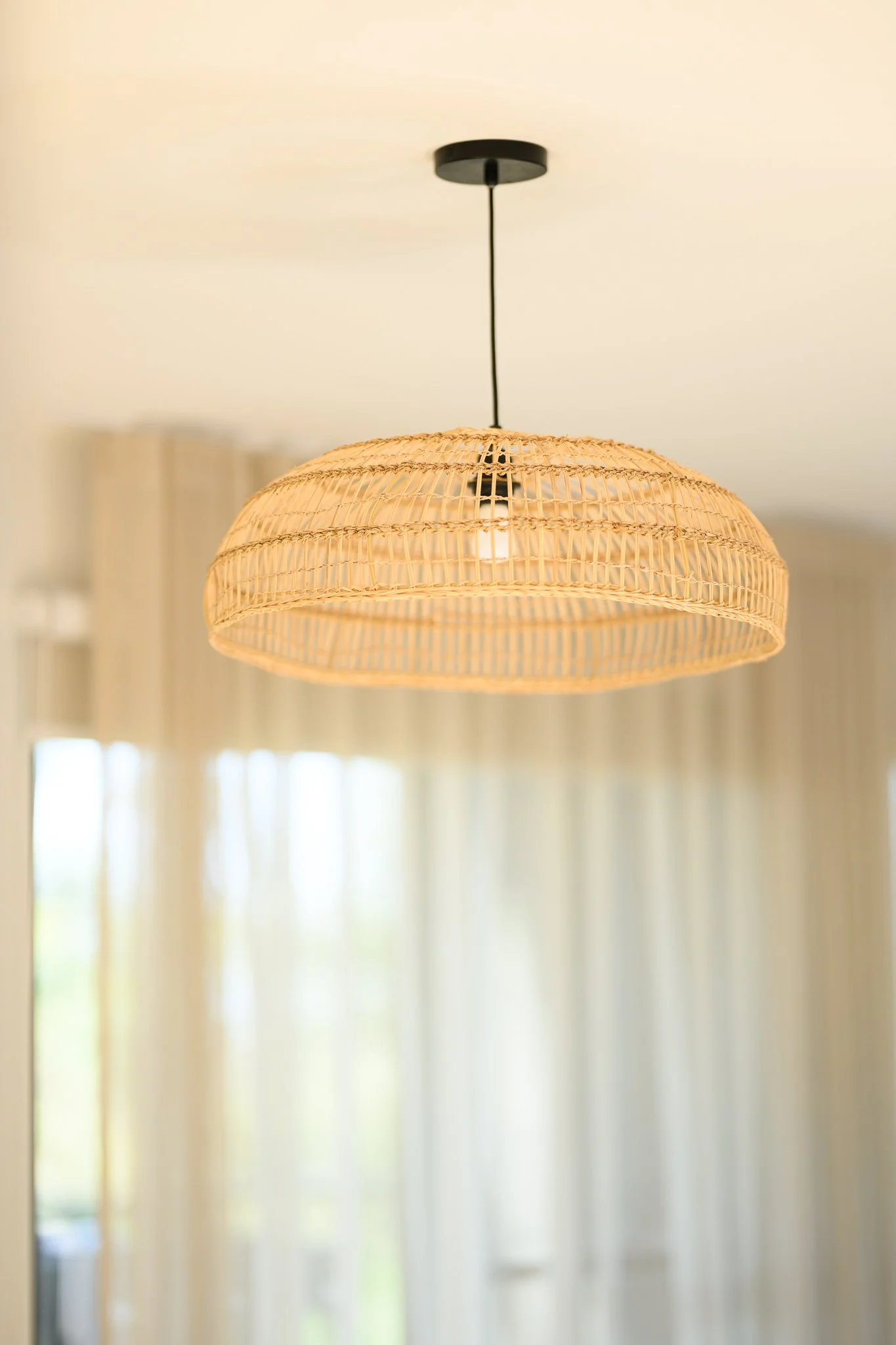 Ceiling light fixture with woven rattan shade hanging in a bright room.