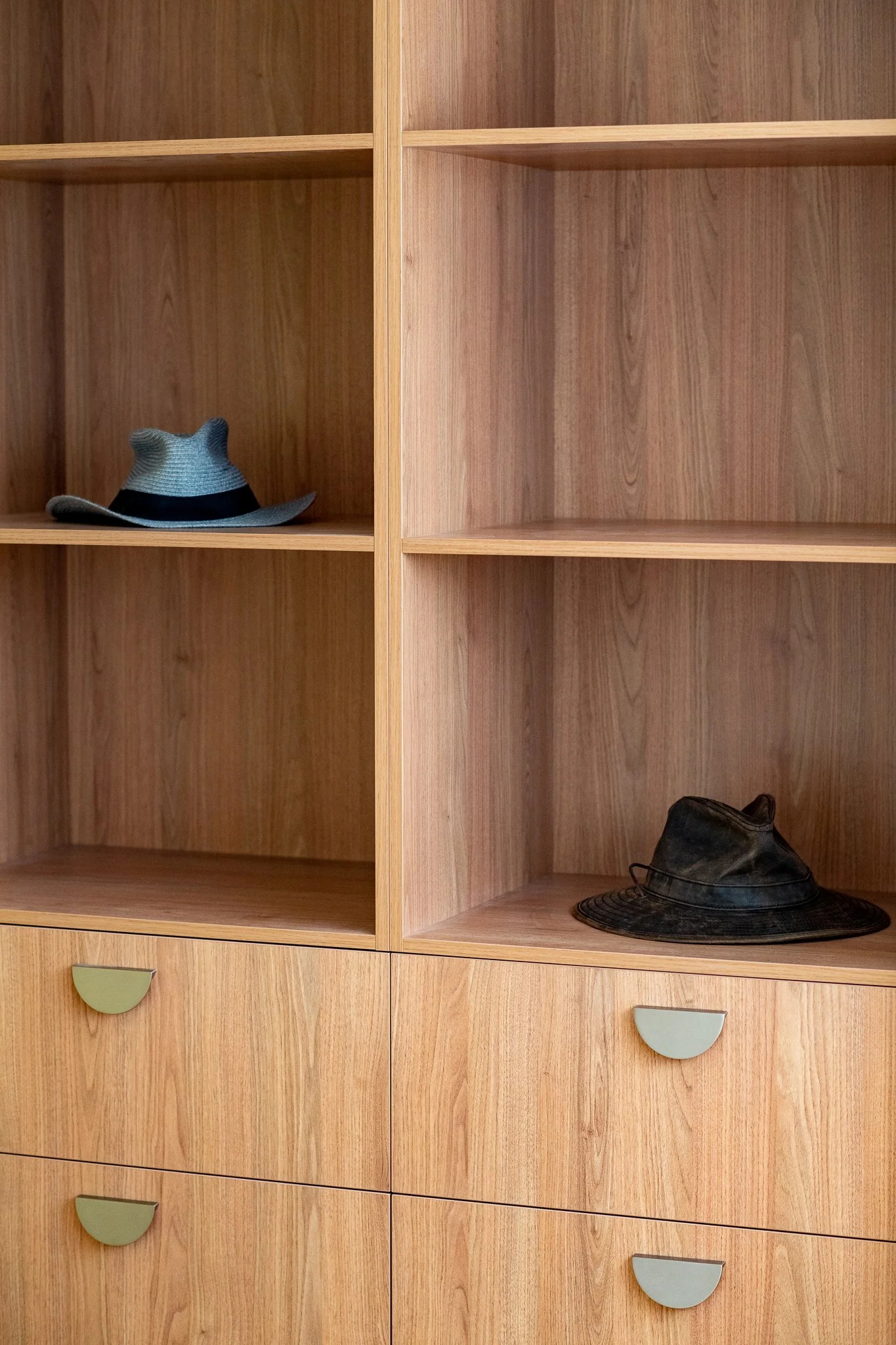 Wooden shelving unit with two hats: a gray woven hat on the middle shelf to the left and a black wide-brimmed hat on the lower right shelf.