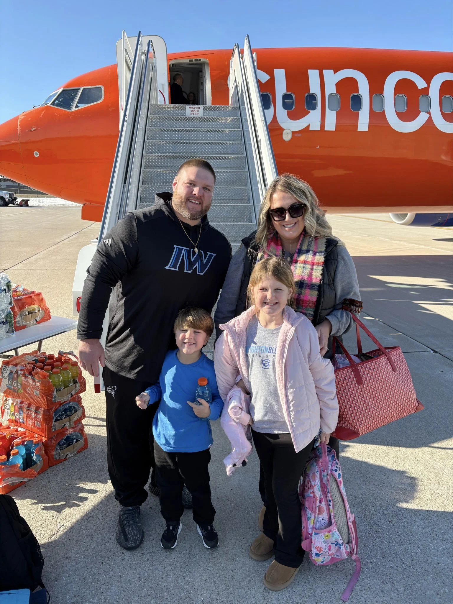 A group of people, including children and two adults, standing in front of an orange Southwest Airlines airplane with an open door and stairway, on a clear day.