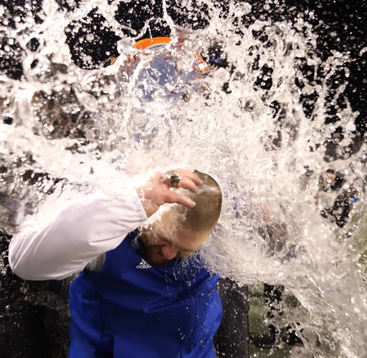 Person in a blue and white jacket smashing a pie tin on their head amid a splash of water.