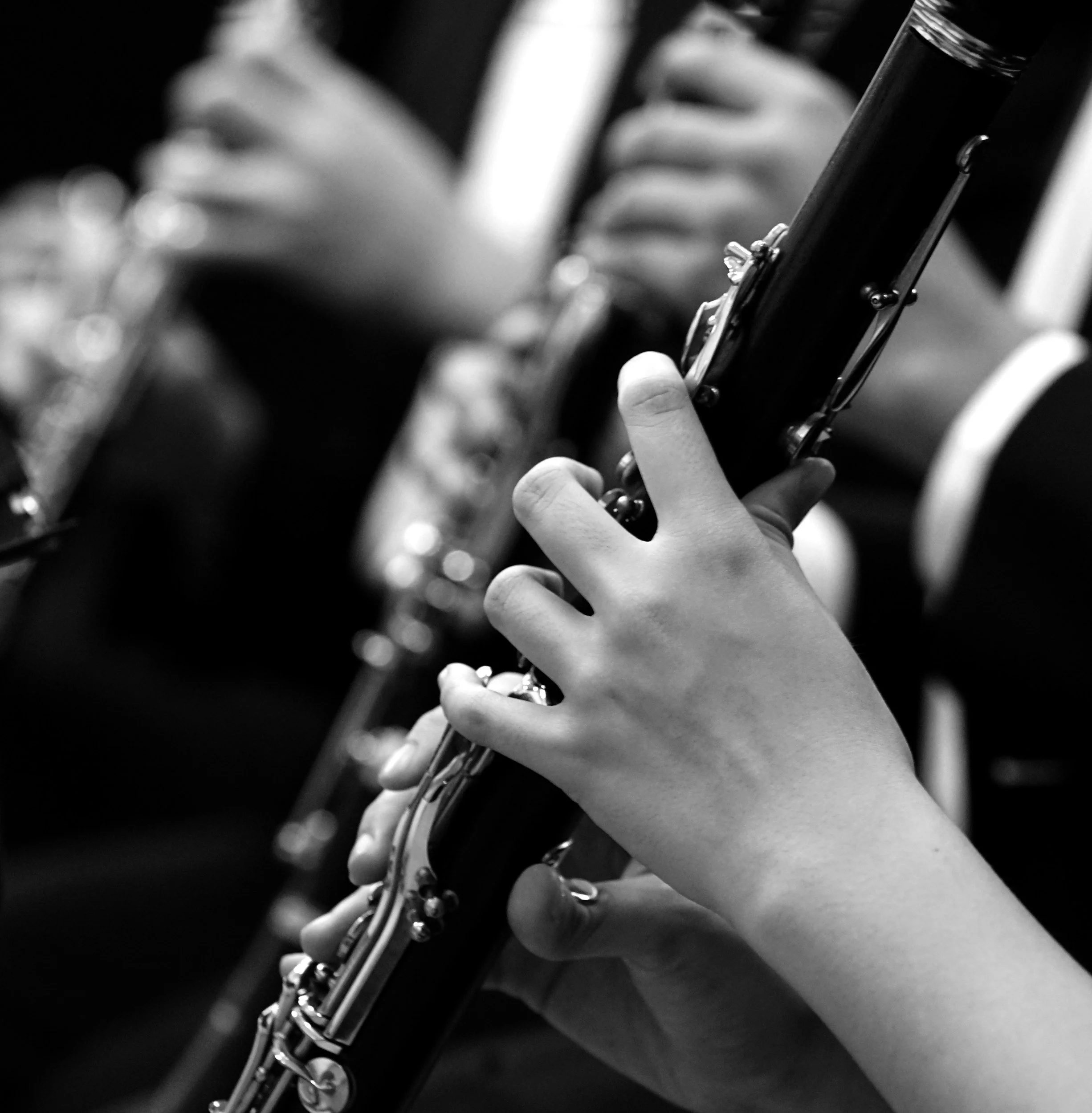 Close-up of a person playing a clarinet, focusing on the hand and the instrument, in black and white.