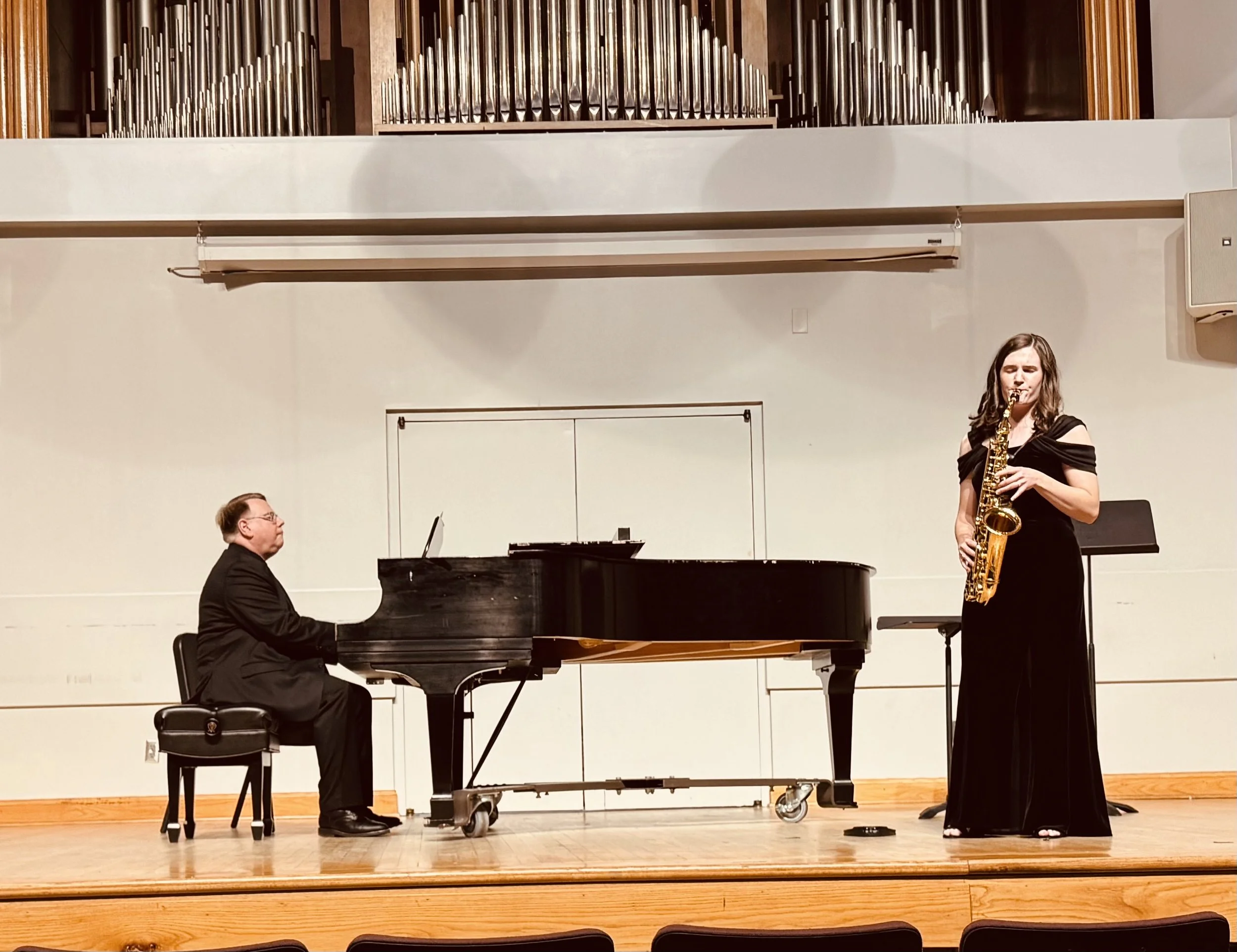 A pianist and a saxophonist performing on stage in a concert hall.