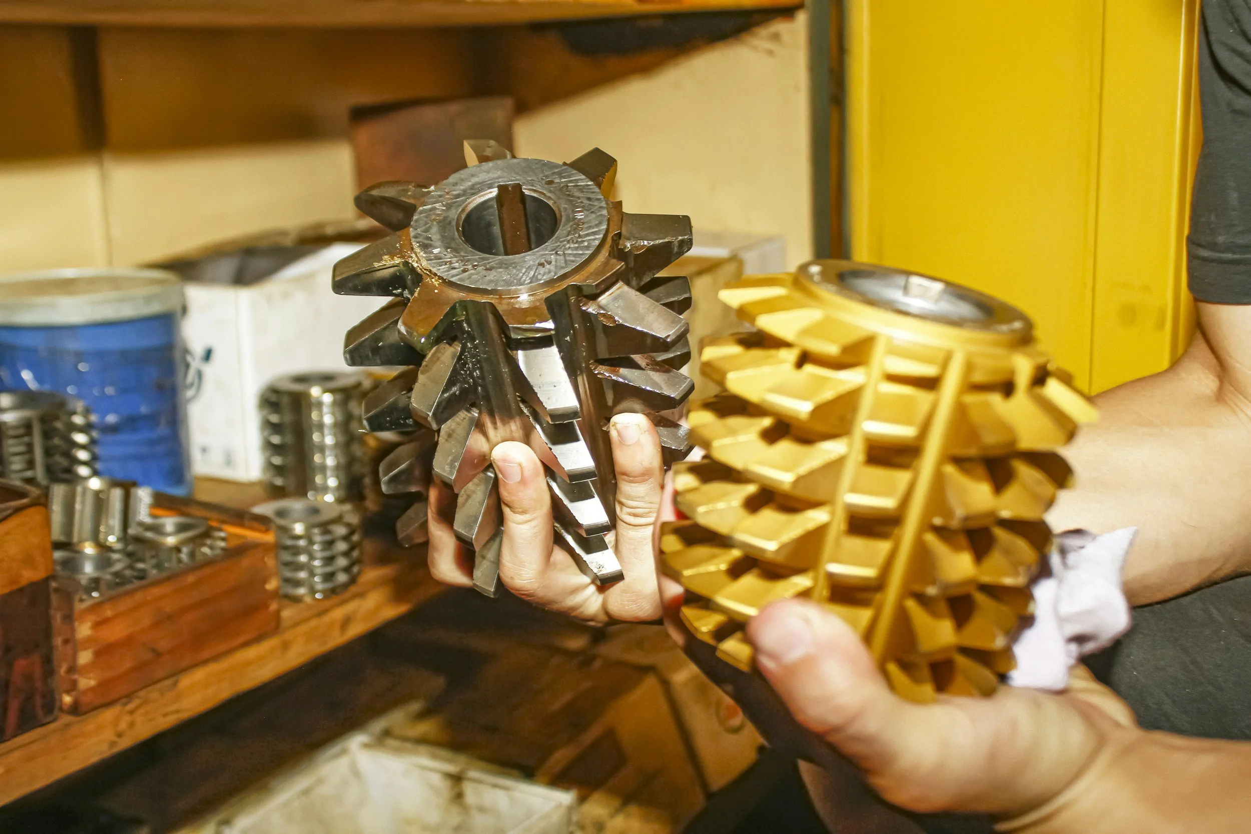 Close-up of a person holding a large metal gear with sharp teeth in a workshop or storage area.