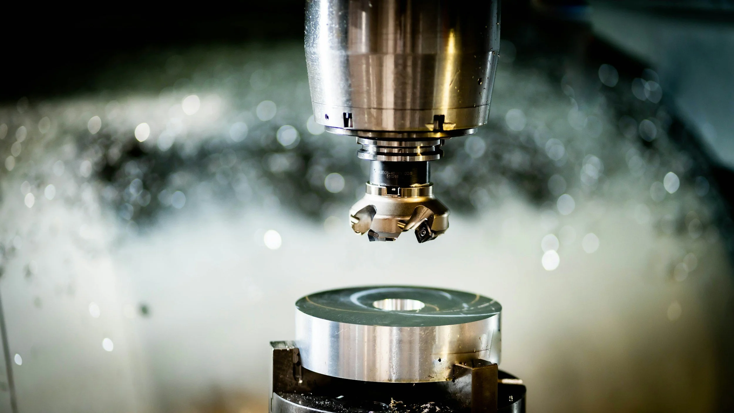 Close-up of a CNC machine cutting or engraving metal, with a sharp cutting tool at the center and metal shavings around.