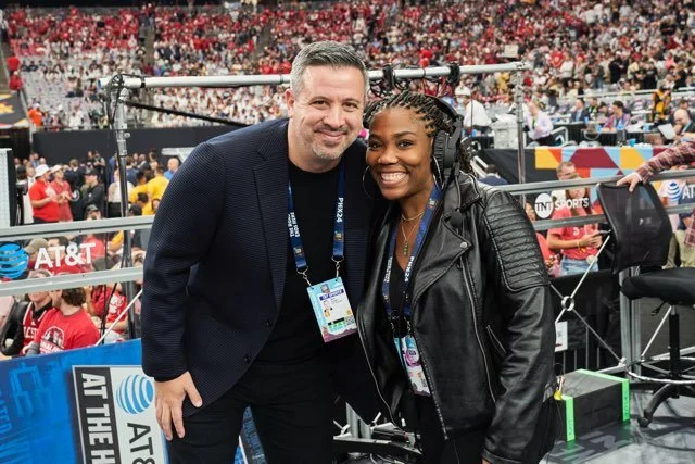 Two people smiling at the camera in a sports arena with a crowd in the background, at an event with AT&T signage.