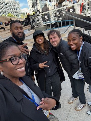 A group of five diverse people smiling and posing for a photo outdoors in an urban setting with stairs and railings in the background.