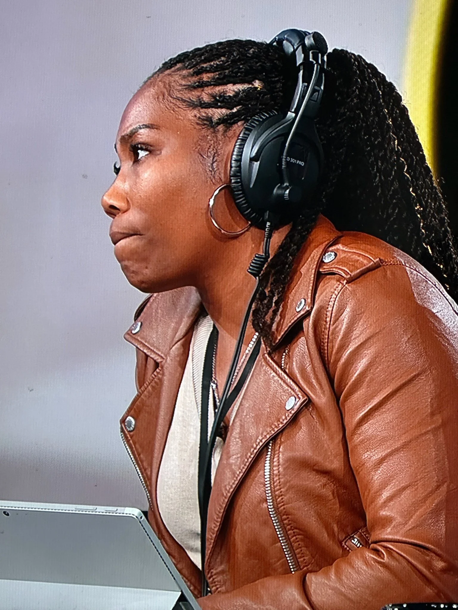 A woman with dreadlocks wearing headphones and a brown leather jacket, working on a tablet.