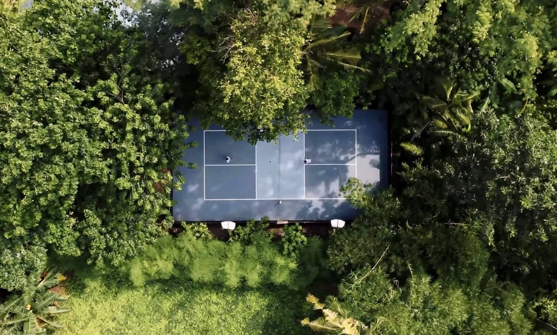 An aerial view of a tennis court surrounded by lush green trees and plants.