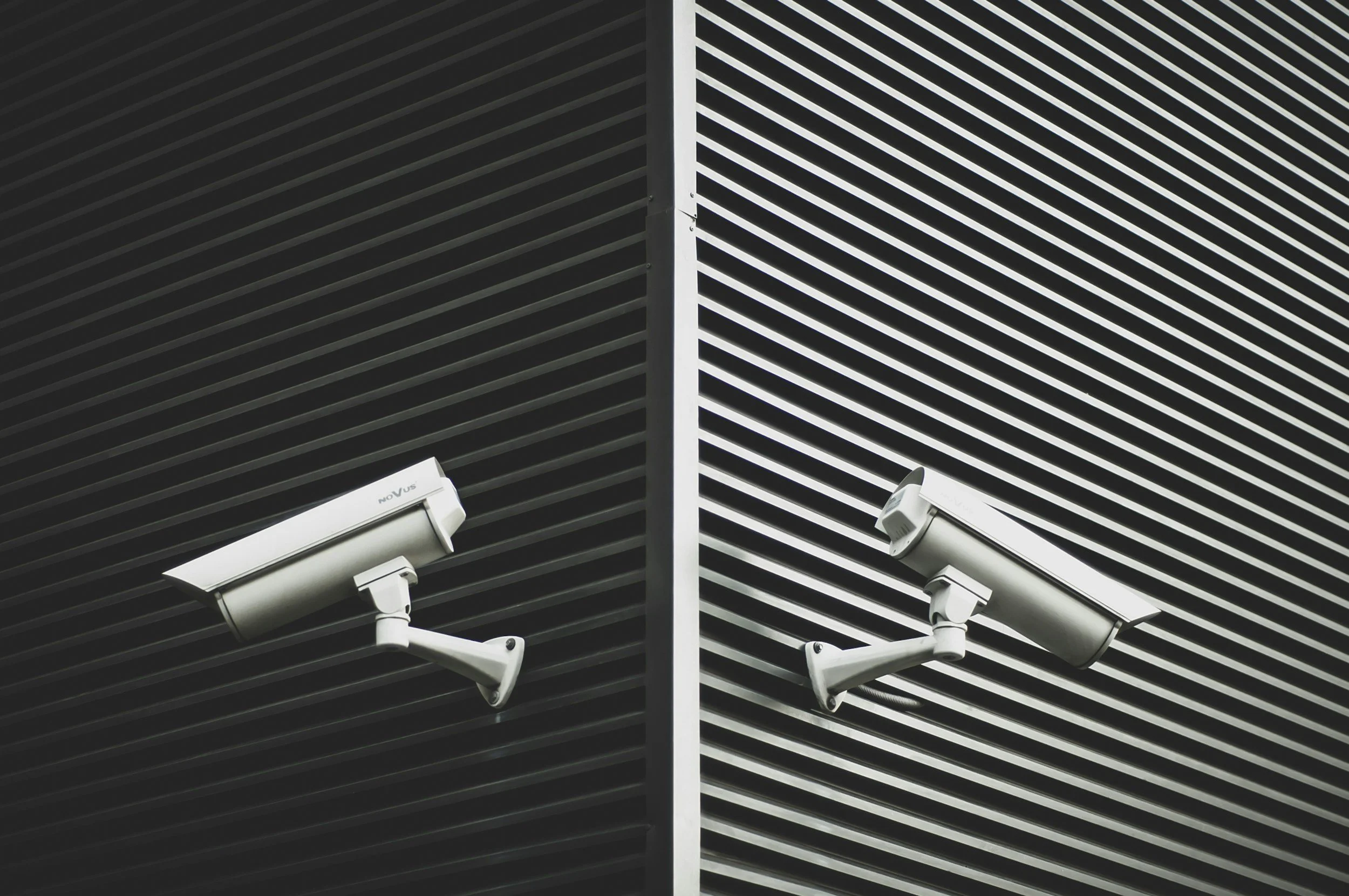Close-up of building exterior with black and white horizontal slatted panels and security cameras attached.