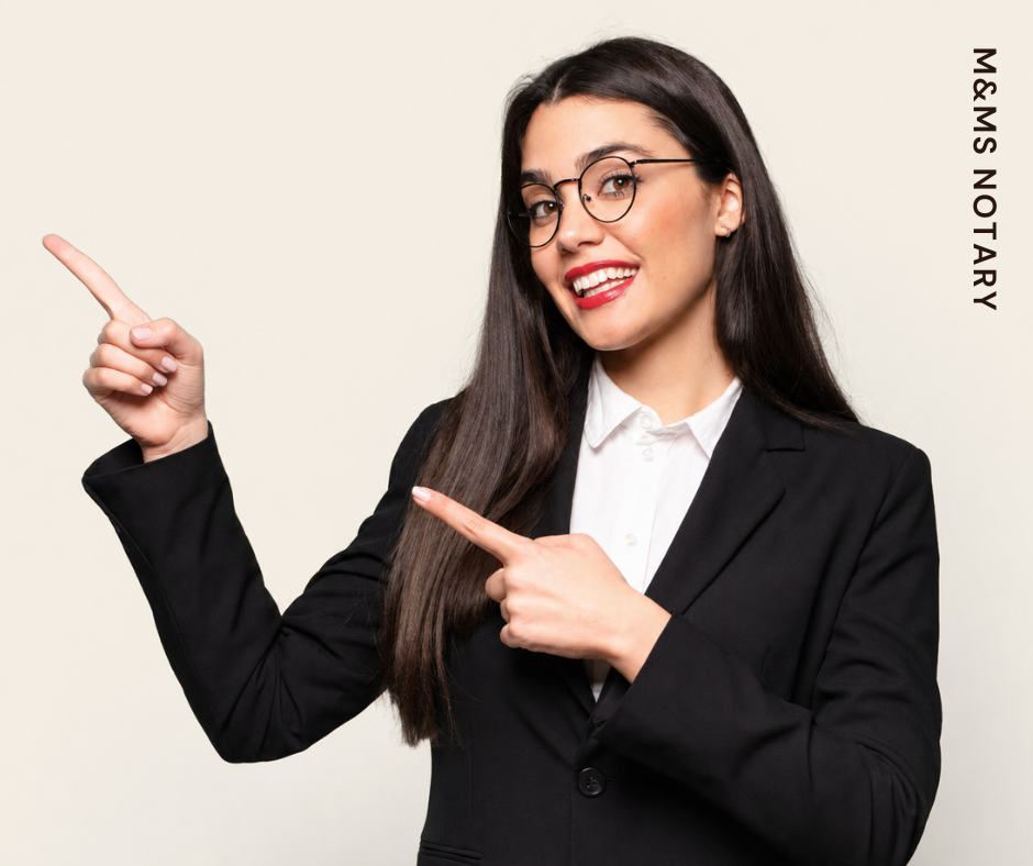 A woman with long dark hair, glasses, and red lipstick, dressed in a black blazer and white shirt, smiling and pointing to her right against a plain light background.