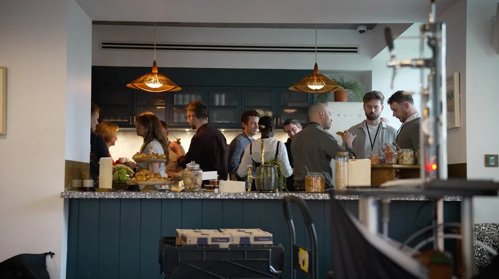 People gathering at a kitchen counter with snacks and drinks in a modern, well-lit space.