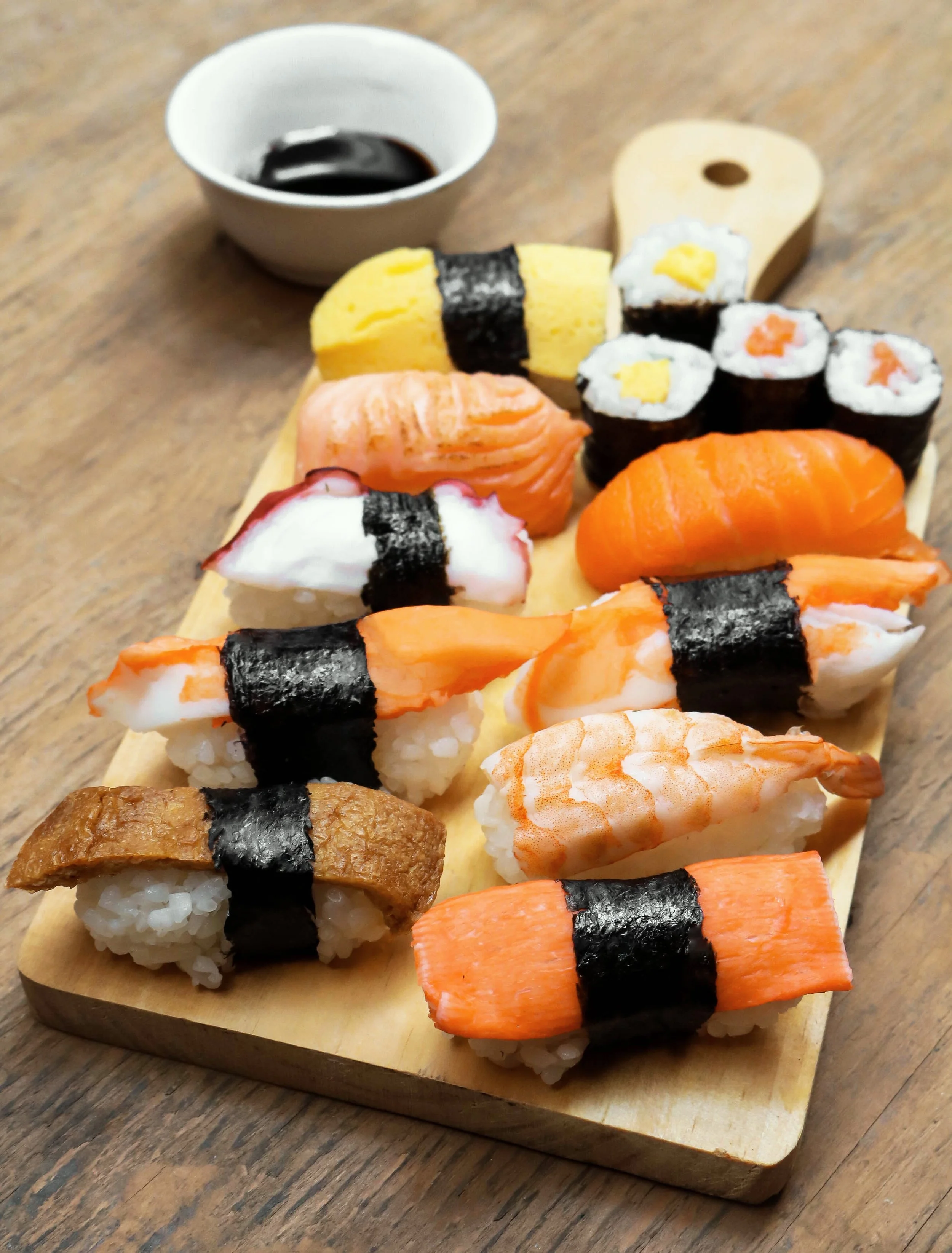 Assorted sushi pieces on a wooden serving board with soy sauce in a small bowl.