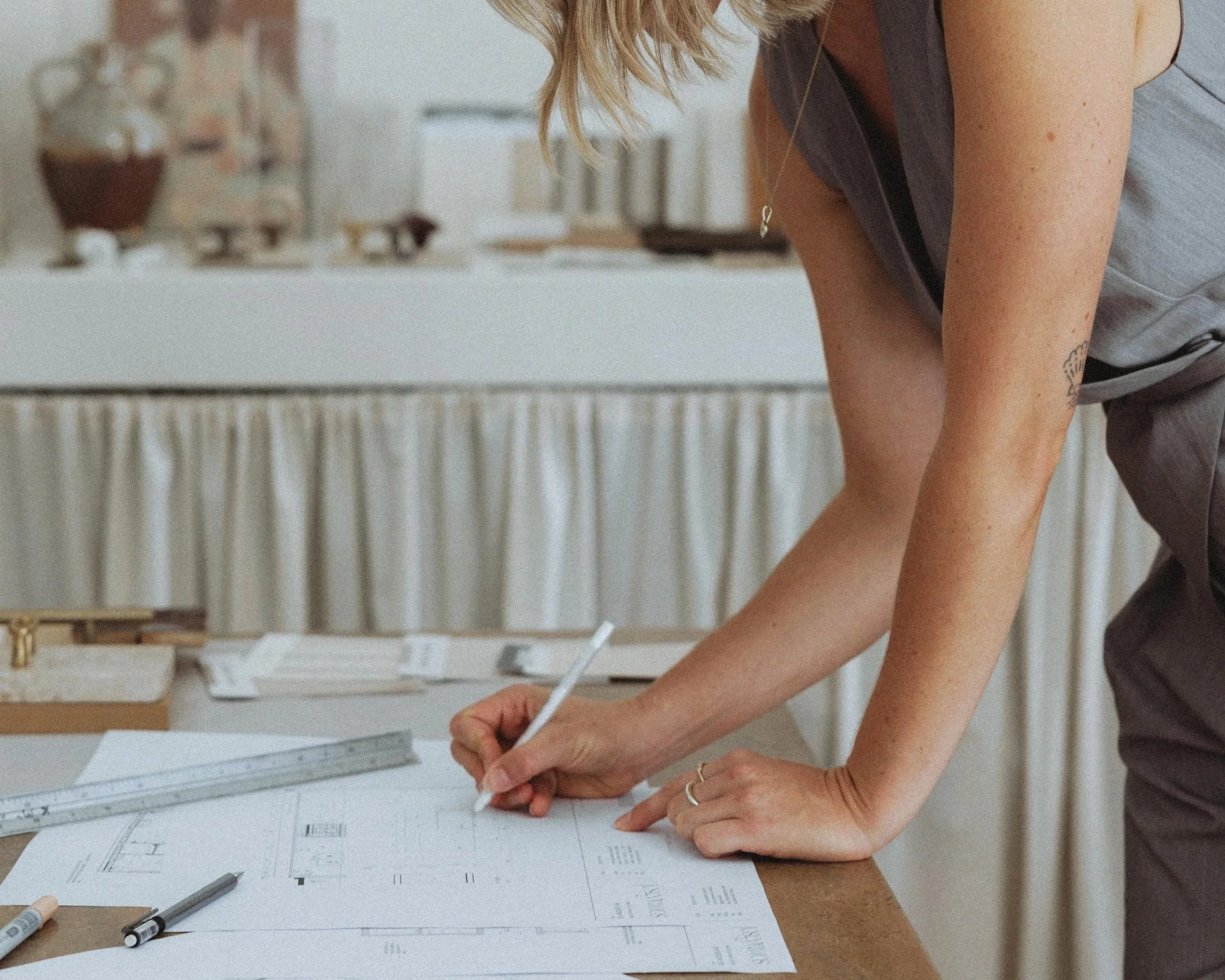 A woman is working on architectural plans at a desk with tools and sketches.