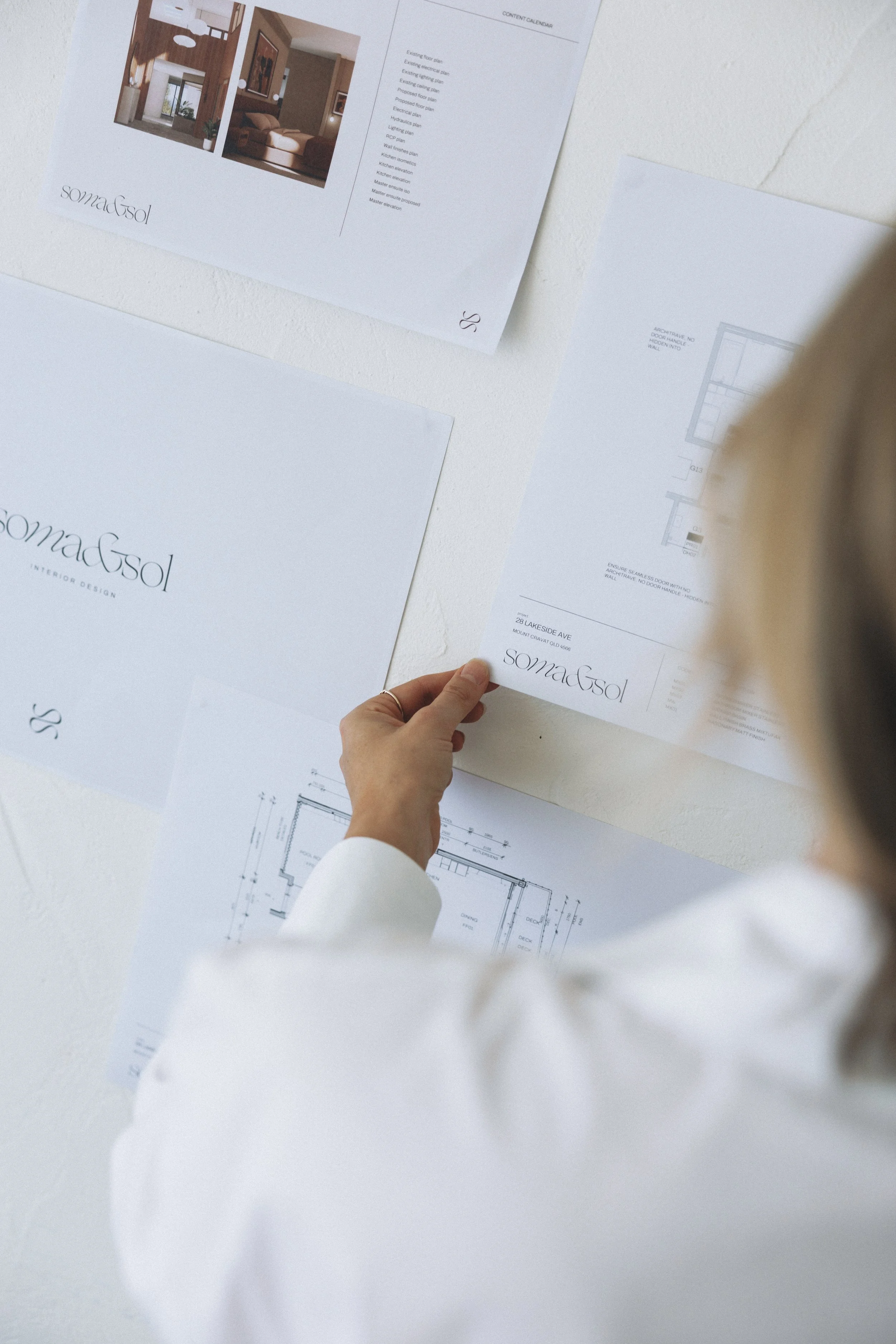 Person holding architectural blueprint with interior design and floor plan layouts laid out on a white surface.