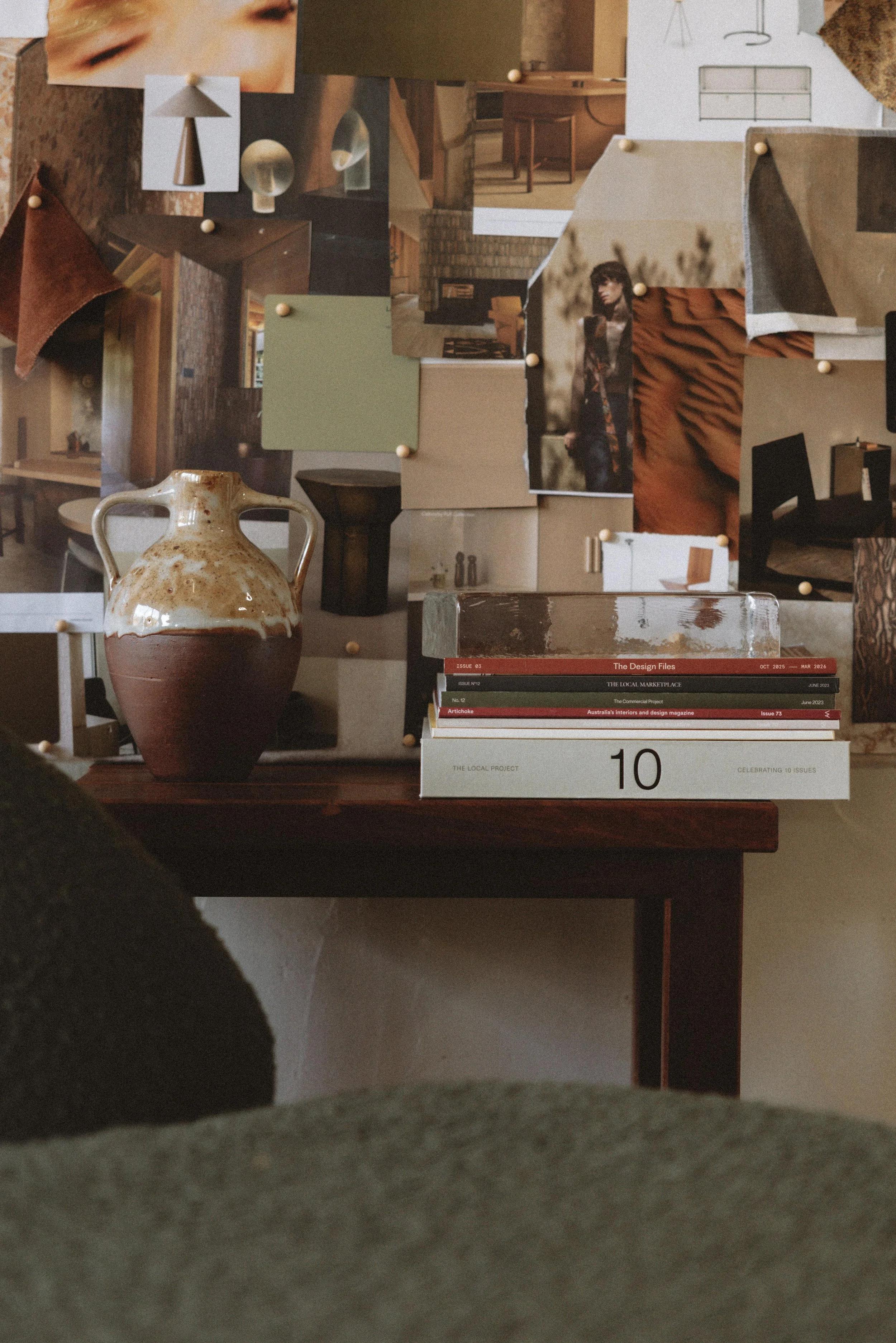 A collage of various photographs, artworks, and objects pinned to a corkboard and a table, including a large vase, books, a framed photo of a woman, and pictures of lamps and people.