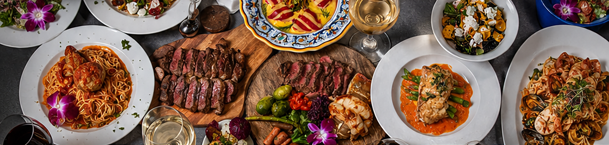 A variety of dishes including pasta, steak, chicken, salads, and a bowl of colorful vegetables, with glasses of white and red wine on a dark table.