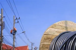 Aerial fiber optic technician climbing utility pole near fiber cable reel during broadband infrastructure installation