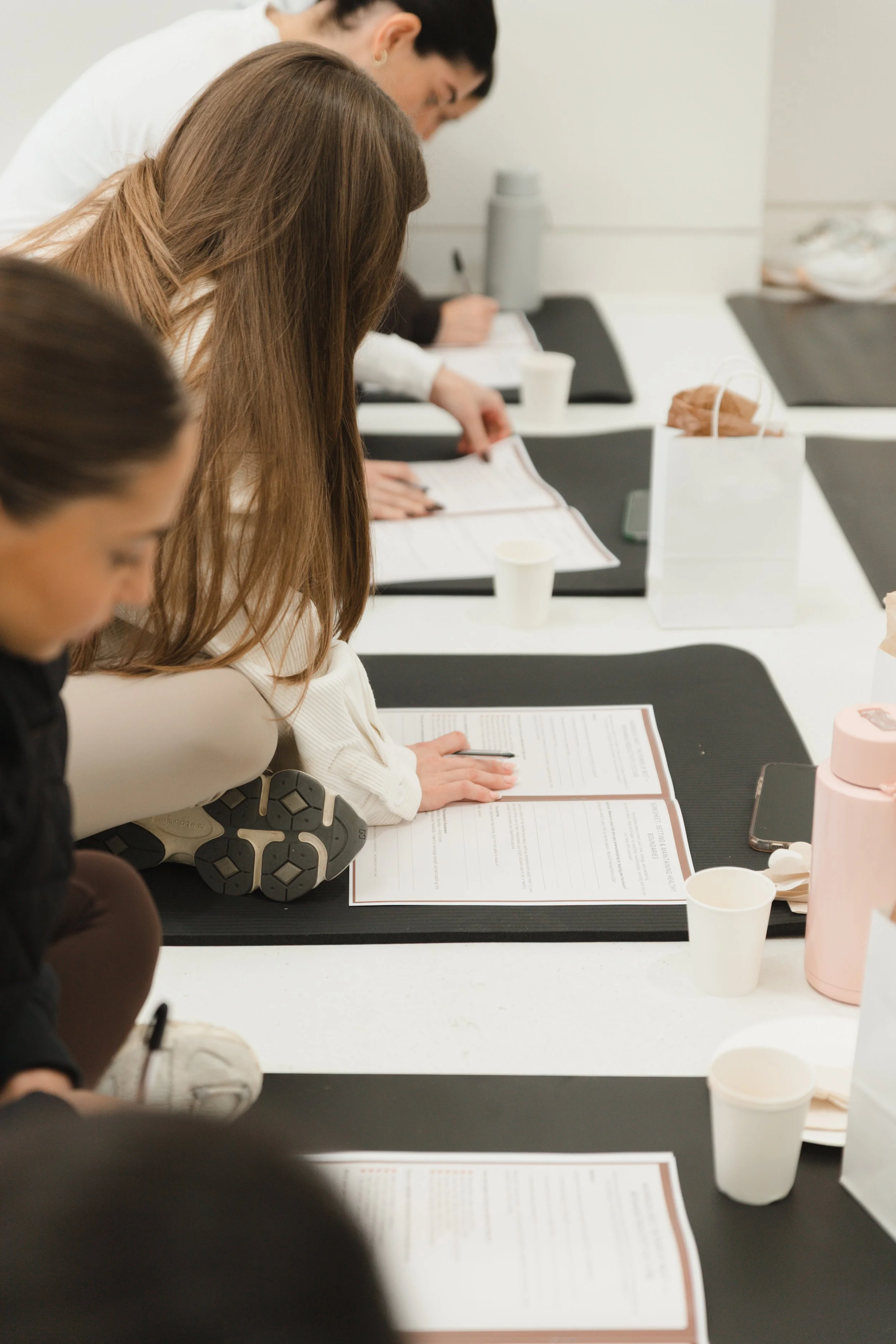People sitting at a table reading documents, with cups, a water bottle, and a gift bag on the table.