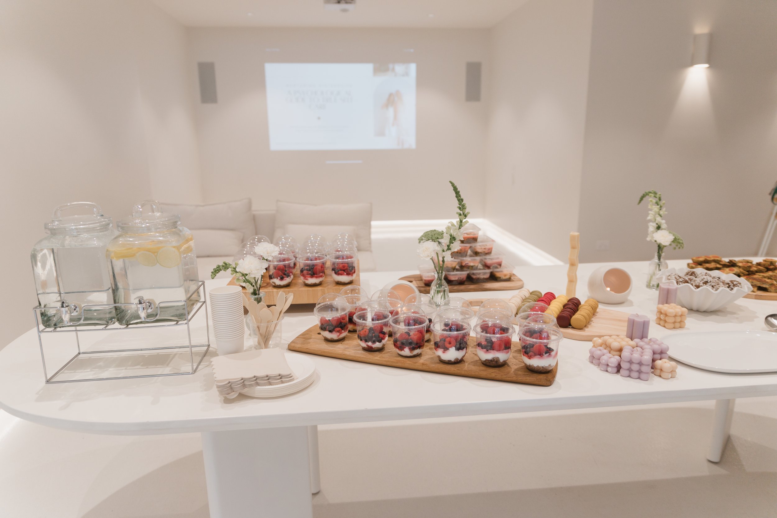 A dessert buffet table with various treats including berry parfaits, macarons, cookies, and chocolates, decorated with small flower arrangements.