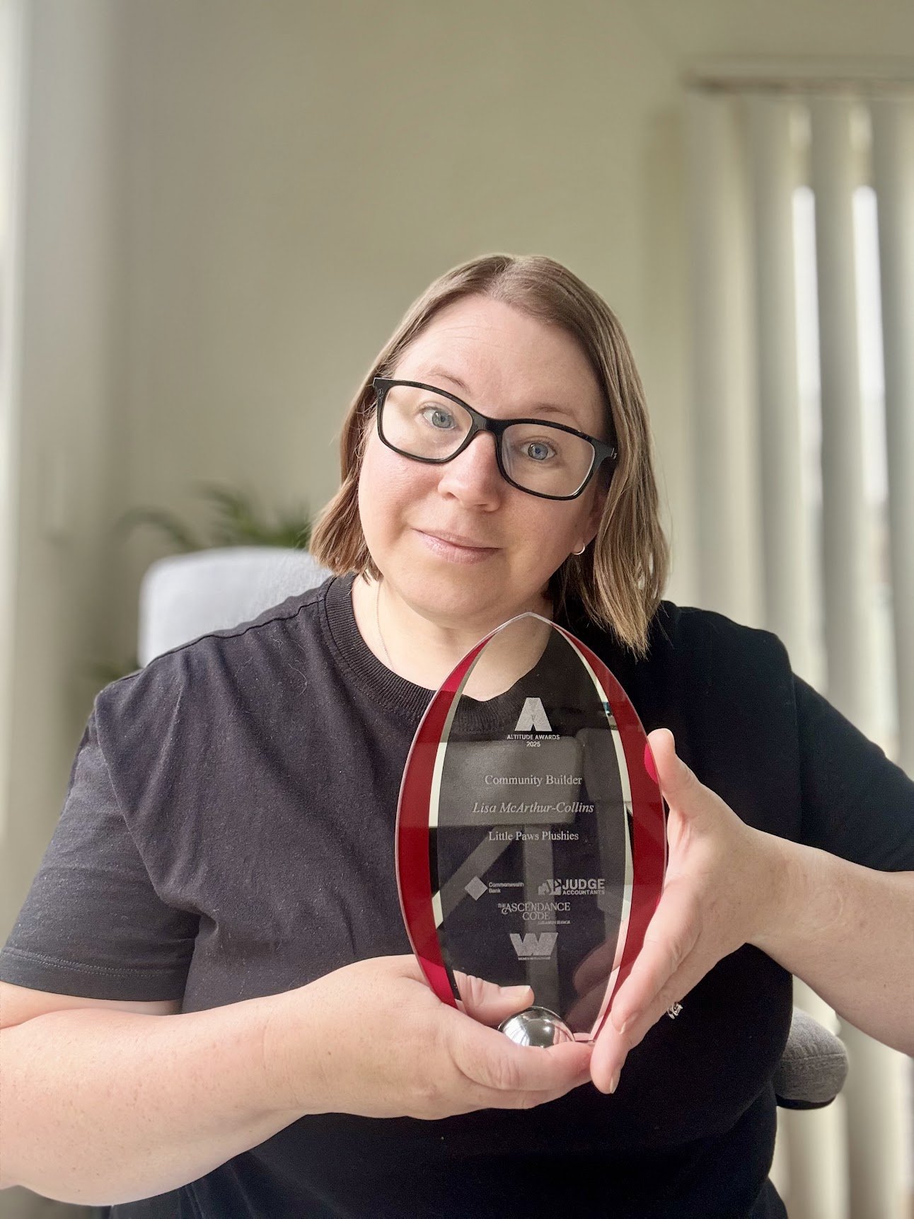 A woman with glasses holding a glass award with a black and red design, inscribed with her achievements and the logo of Judge Accountant.