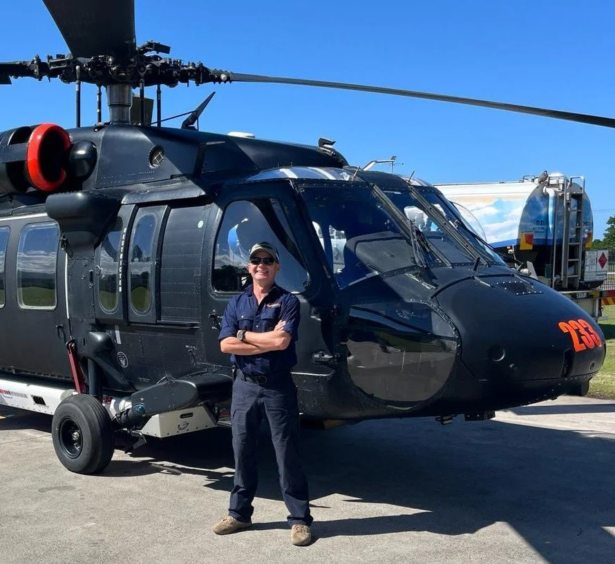 Person standing in front of a black helicopter outdoors on a clear, sunny day.