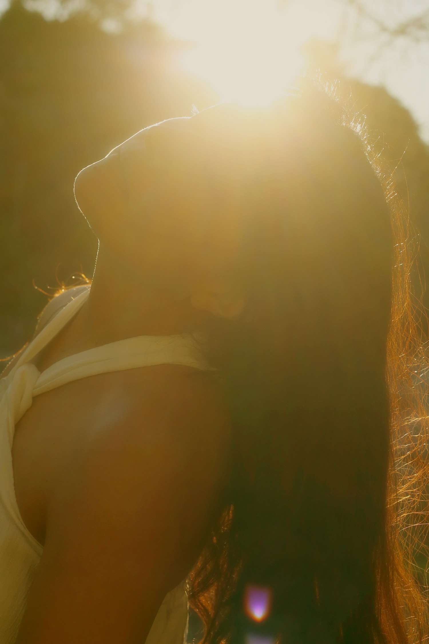 Close-up of a person's shoulder and neck with sunlight in the background, creating a warm glow and lens flare.