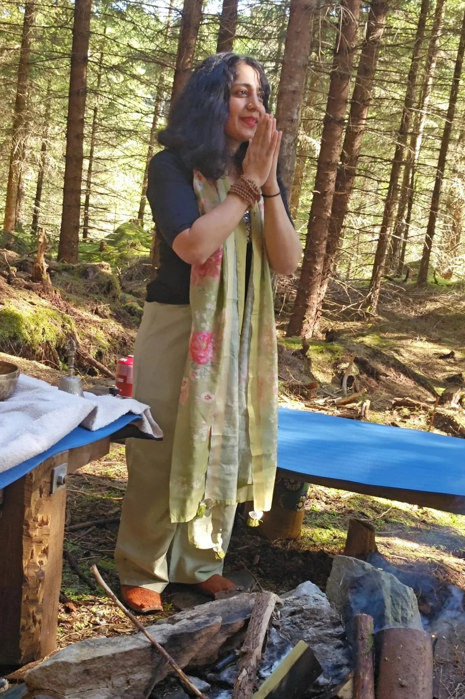 Woman standing in a forest with her hands in a prayer position during a spiritual or meditation session.