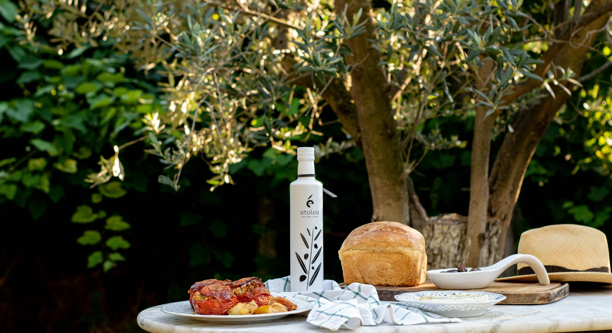 Mediterranean table with food, bread, and olive oil beneath an olive tree, representing nourishment and the Mediterranean way of eating