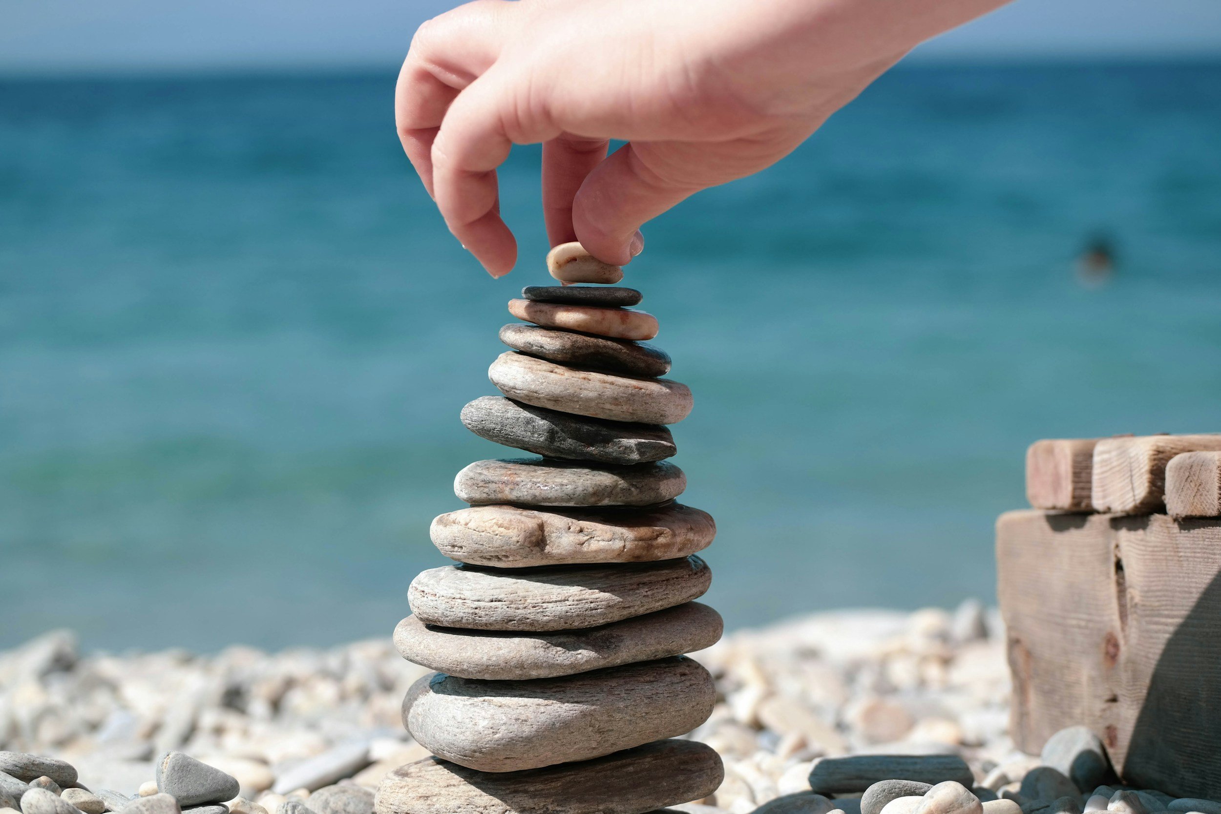 Hand stacking balanced stones on a pebble beach by the sea