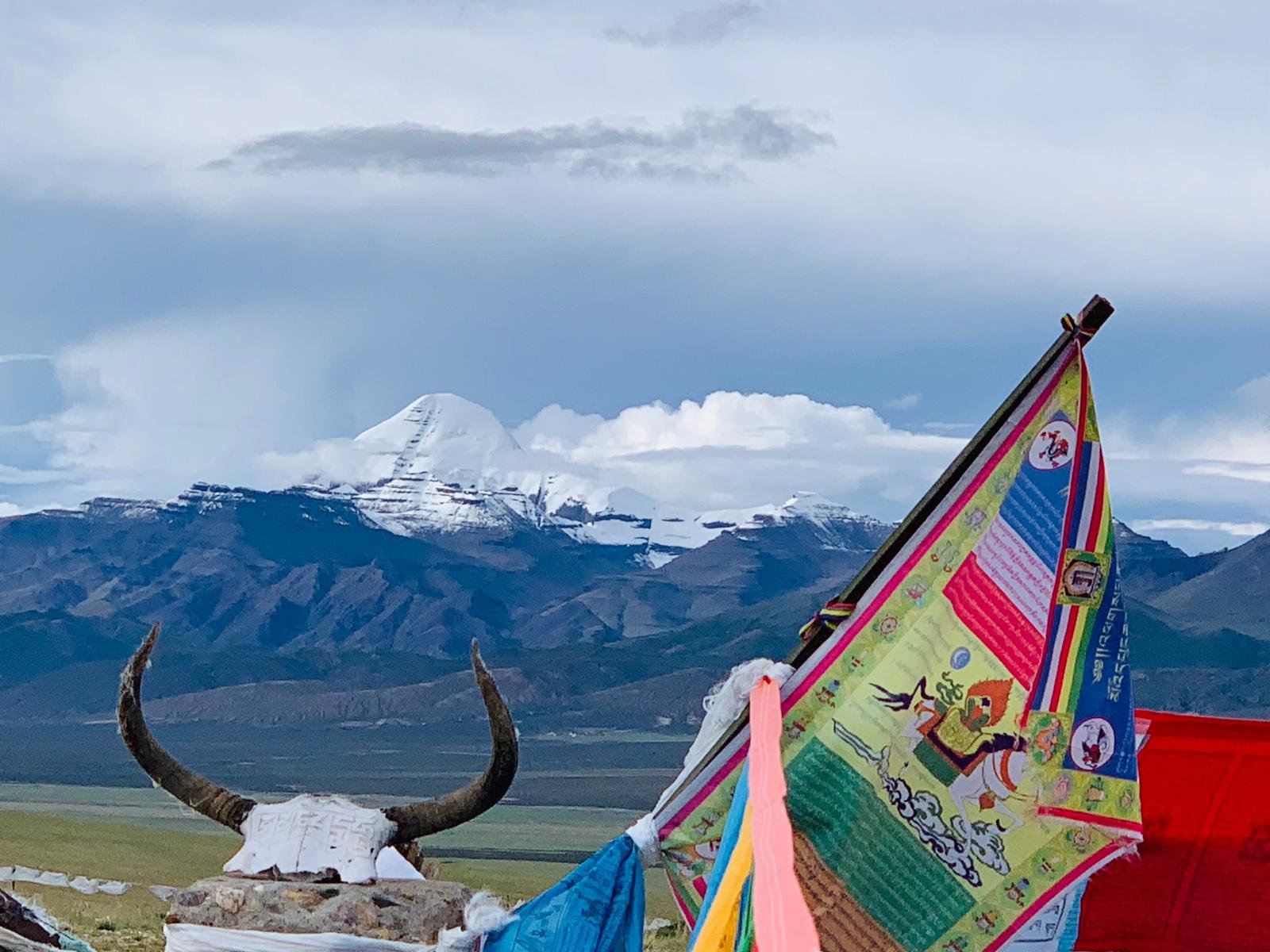 Colorful prayer flags fluttering in front of snow-capped mountains under a cloudy sky.