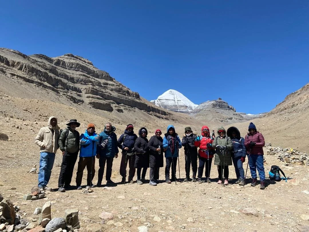 Group of hikers posing in a mountainous desert landscape with Mount Kailash in the background.
