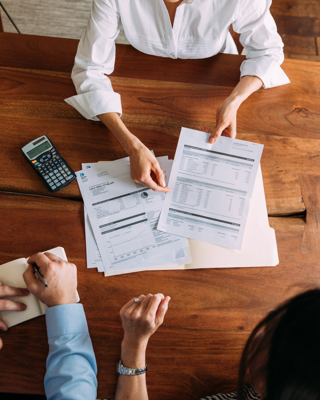 A person in a white shirt discussing financial documents, with a calculator on a wooden table, during a meeting.