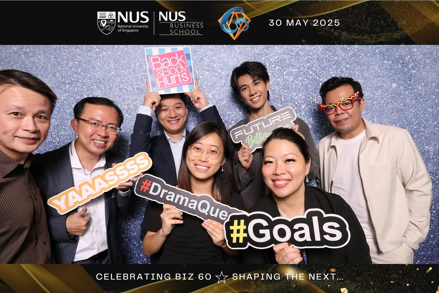 Group of eight diverse people at a celebration event, holding colorful signs with hashtags and phrases, standing in front of a sparkly blue backdrop, with a black and gold border at the top that includes the logos of the National University of Singapore and their Business School, date May 30, 2025, and the phrase 'Celebrating Biz 60 ☆ Shaping the Next...' at the bottom.