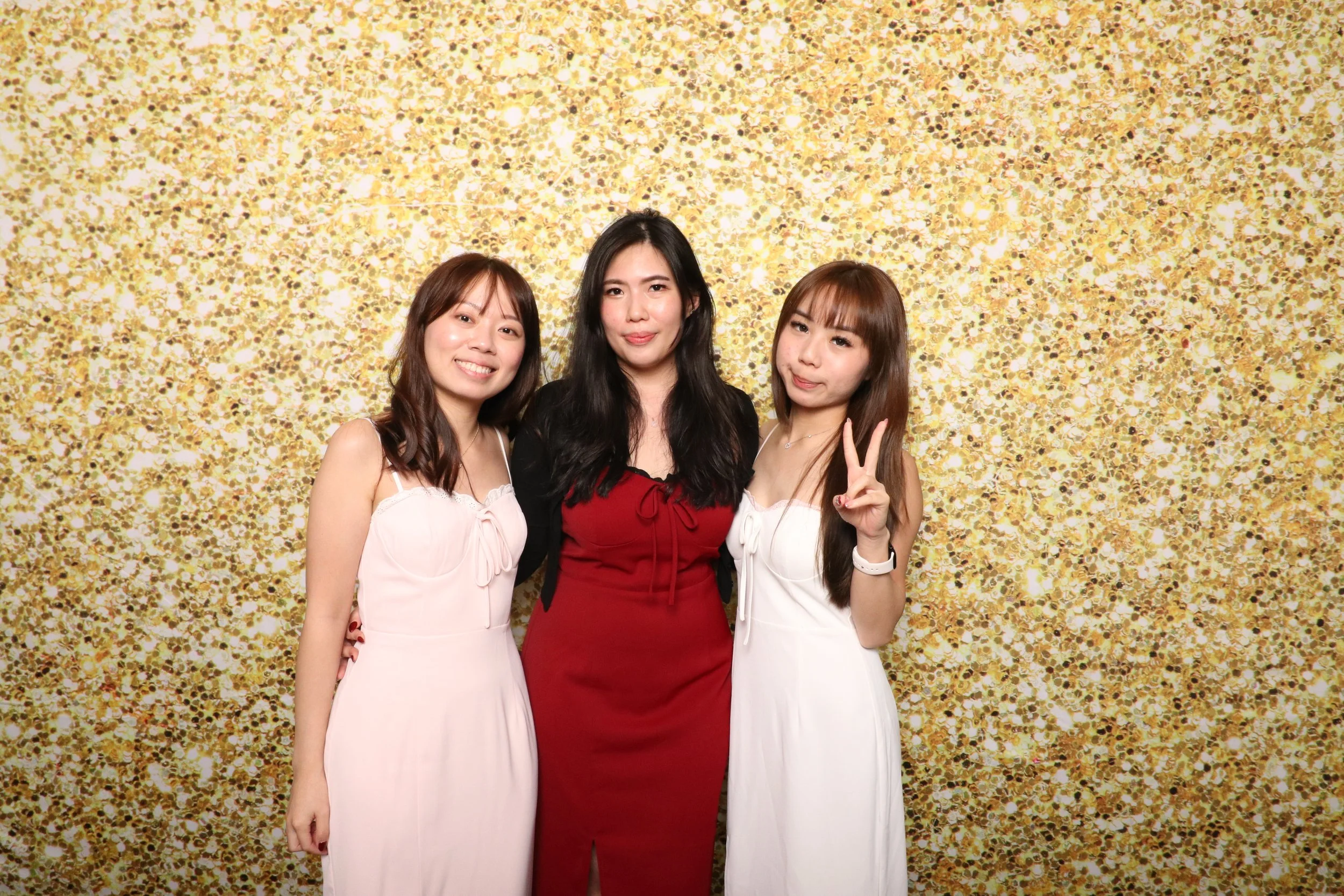 Three women posing in front of a glittery gold background, smiling and making playful gestures.