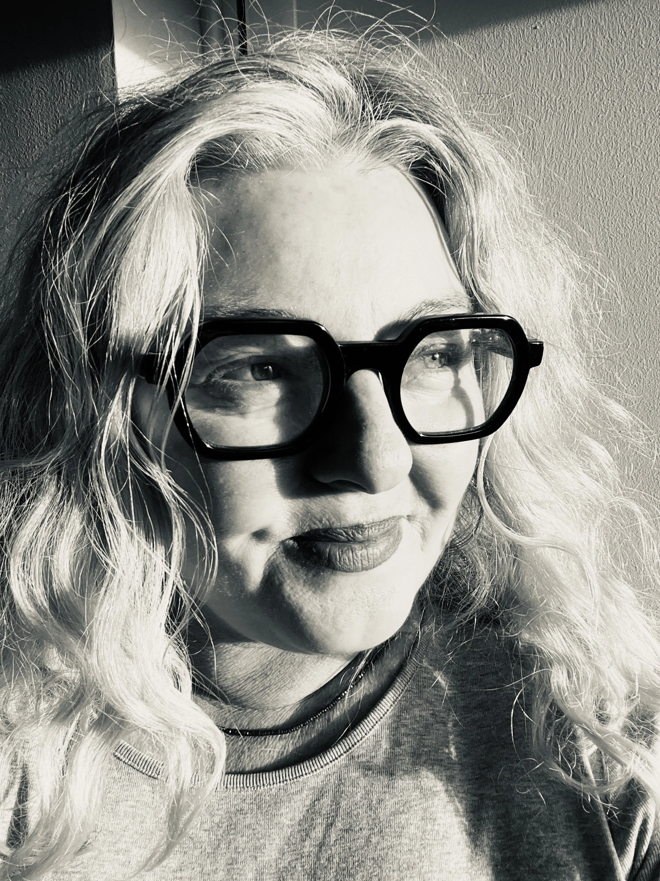Close-up black and white photo of a woman with long wavy hair and glasses, looking downward.