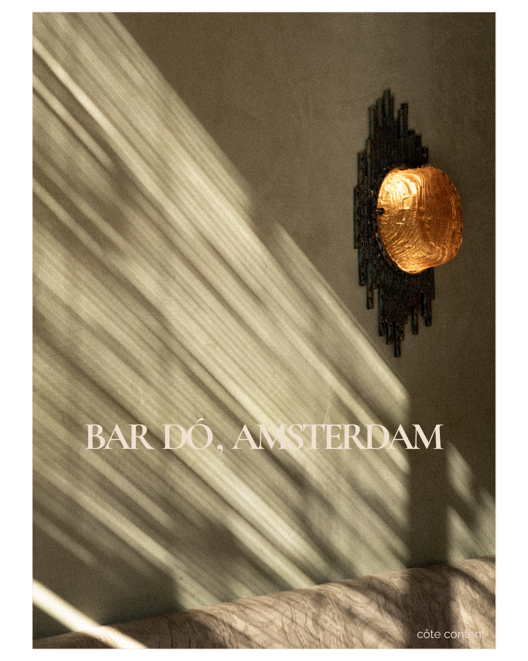 Interior view of a beige wall with ornate gold and black decorative wall lamp, with sunlight casting shadows on the wall. Text overlay reads 'Bar DÓ, Amsterdam' and 'côte content'.