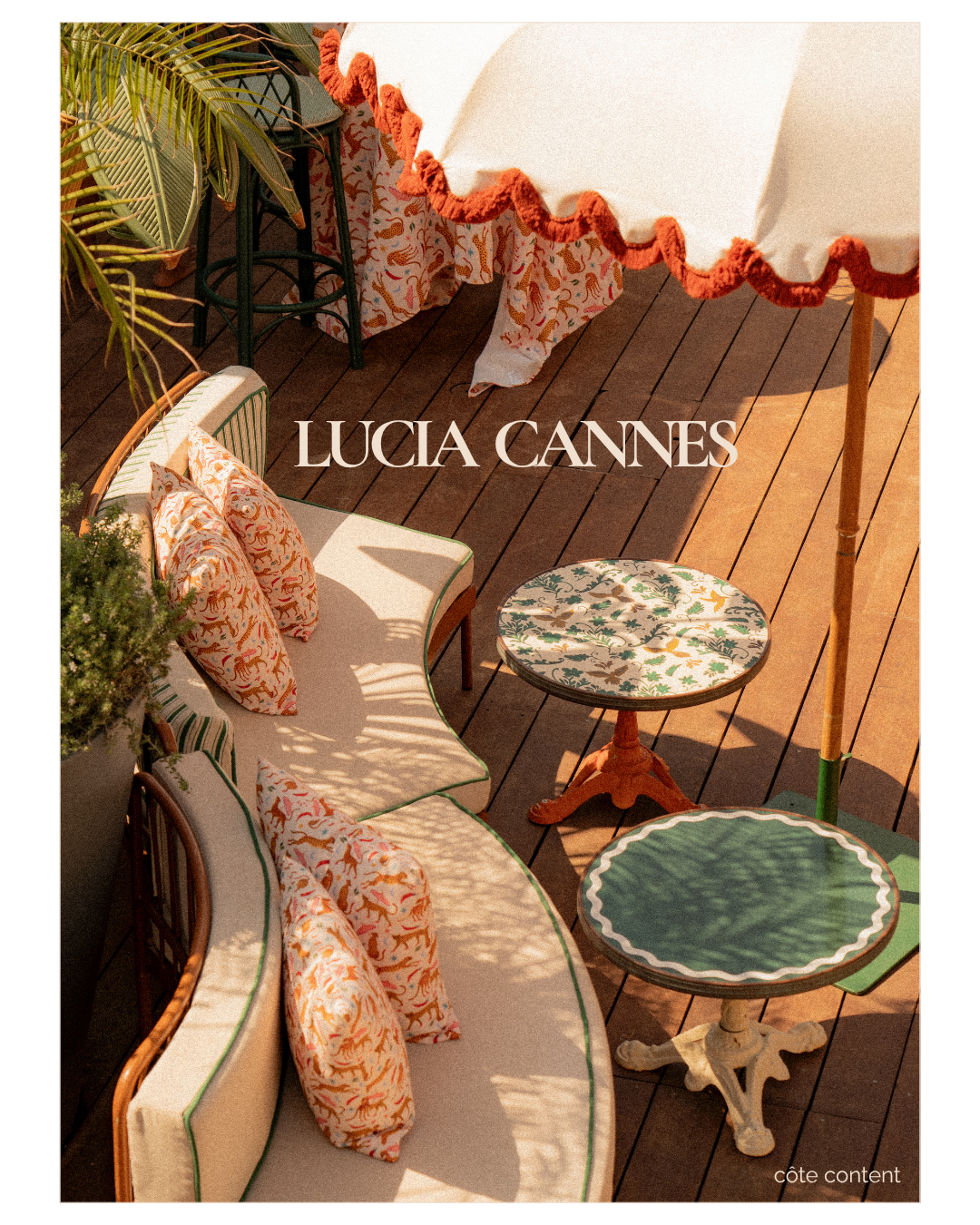 Outdoor patio scene with vintage-style furniture, patterned cushions, and tables, shaded by a large umbrella, with shadows cast on wooden decking.