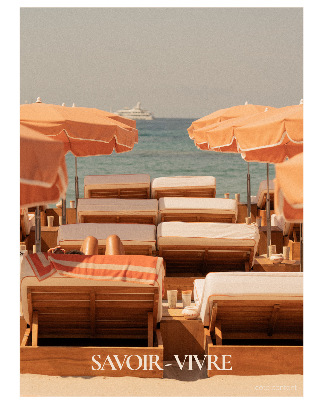 Beach chairs with orange umbrellas facing the ocean, with a yacht in the distance, and the text 'SAVOIR-VIVRE' at the bottom.