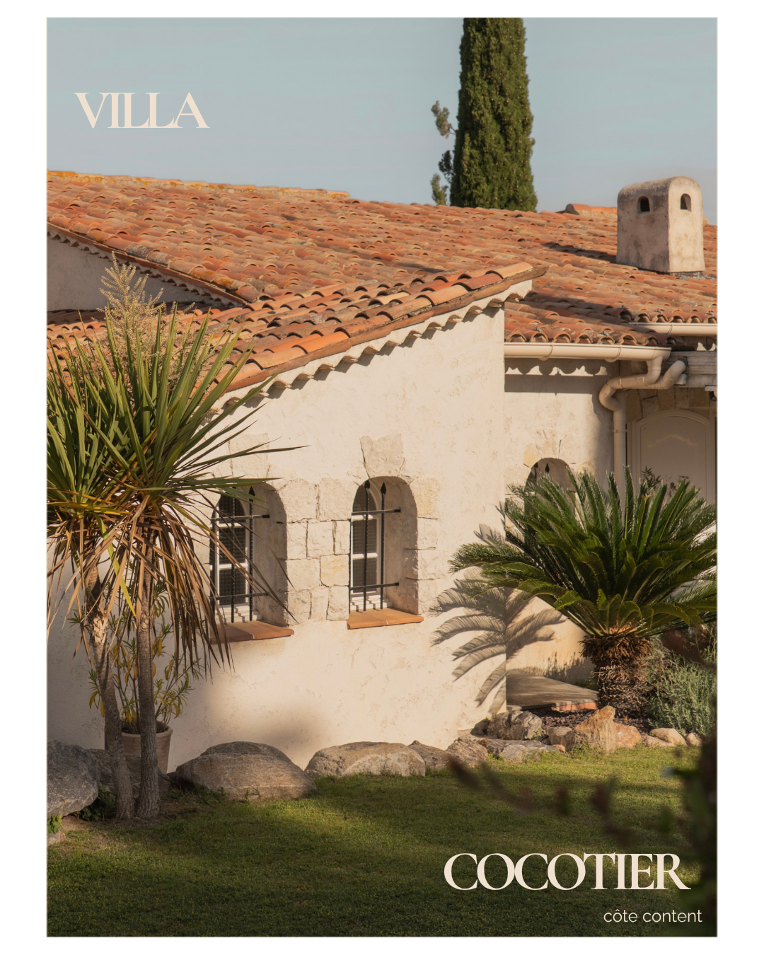 A Mediterranean-style villa with a terracotta tile roof, white stucco walls, and small arched windows protected by bars. The foreground features palm trees and rocks on a well-kept lawn.