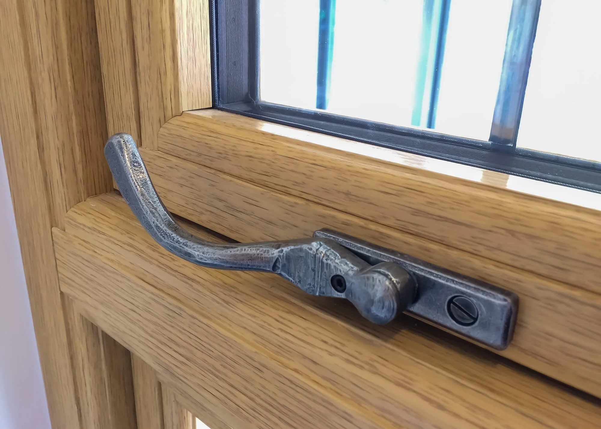 Close-up of a metal window latch on a wooden window frame.