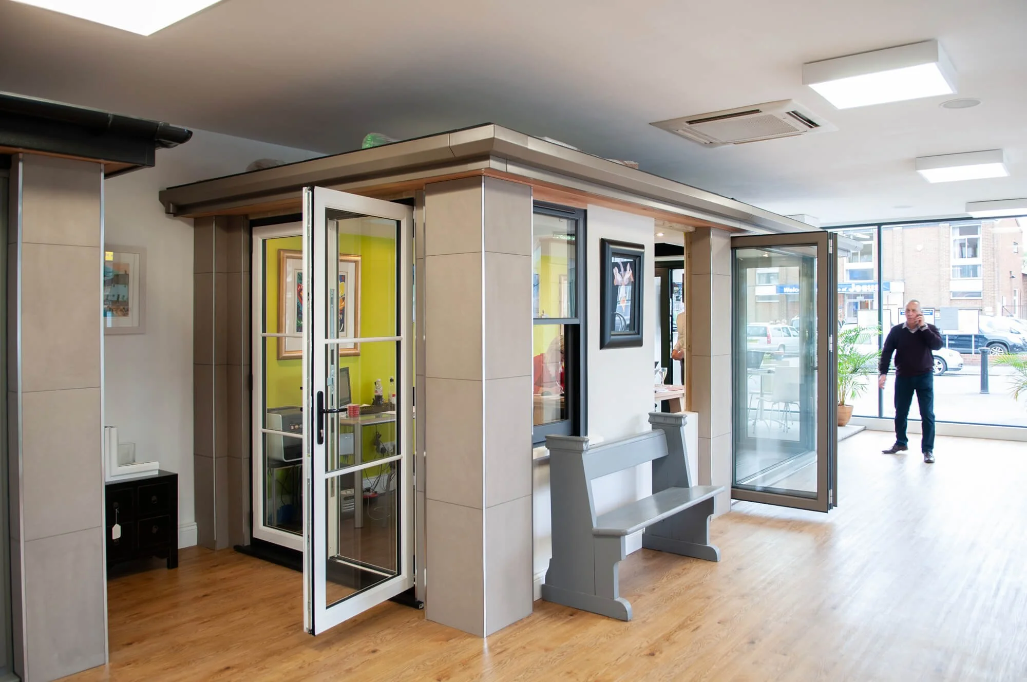 Interior of a modern building with glass doors, a wooden bench, and a man talking on his phone near the entrance.